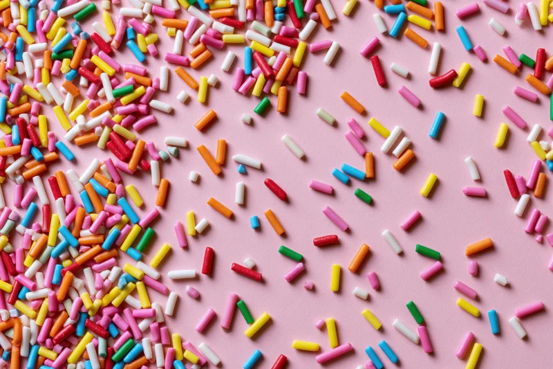 Colorful candy sprinkles scattered randomly across a flat pink surface
