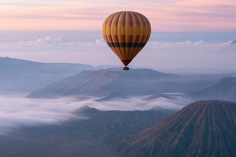 Colorful striped hot air balloon floating above volcanic mountains at sunrise