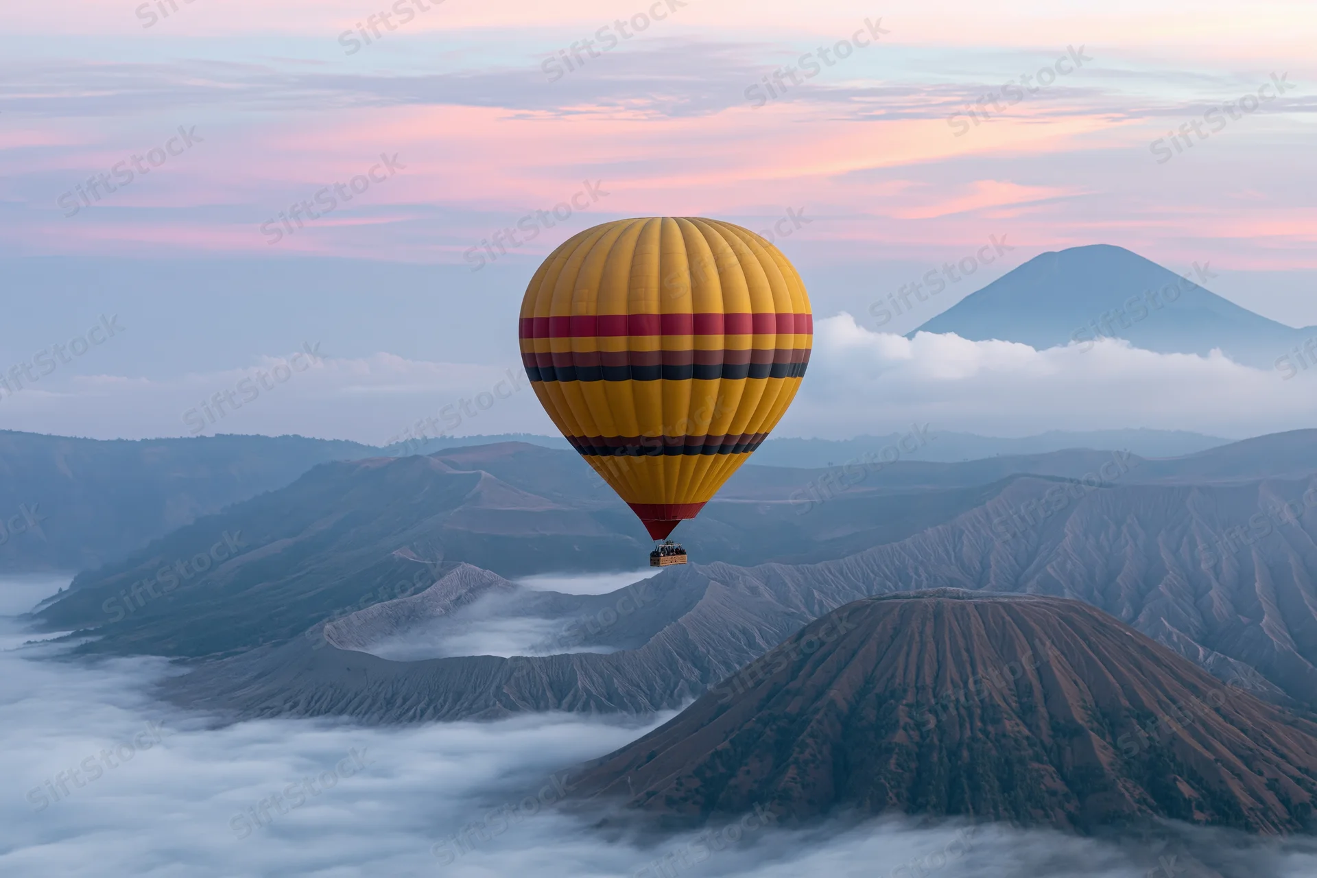 Colorful striped hot air balloon drifting above volcanic mountains at sunrise
