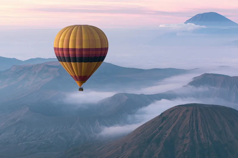 Colorful striped hot air balloon drifting above volcanic mountains at sunrise