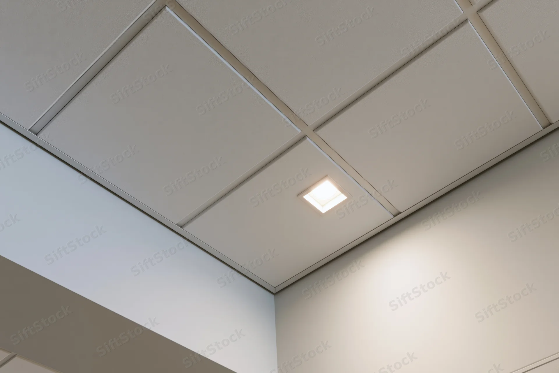Corner junction of a modern office drop ceiling with recessed lighting and white tiles