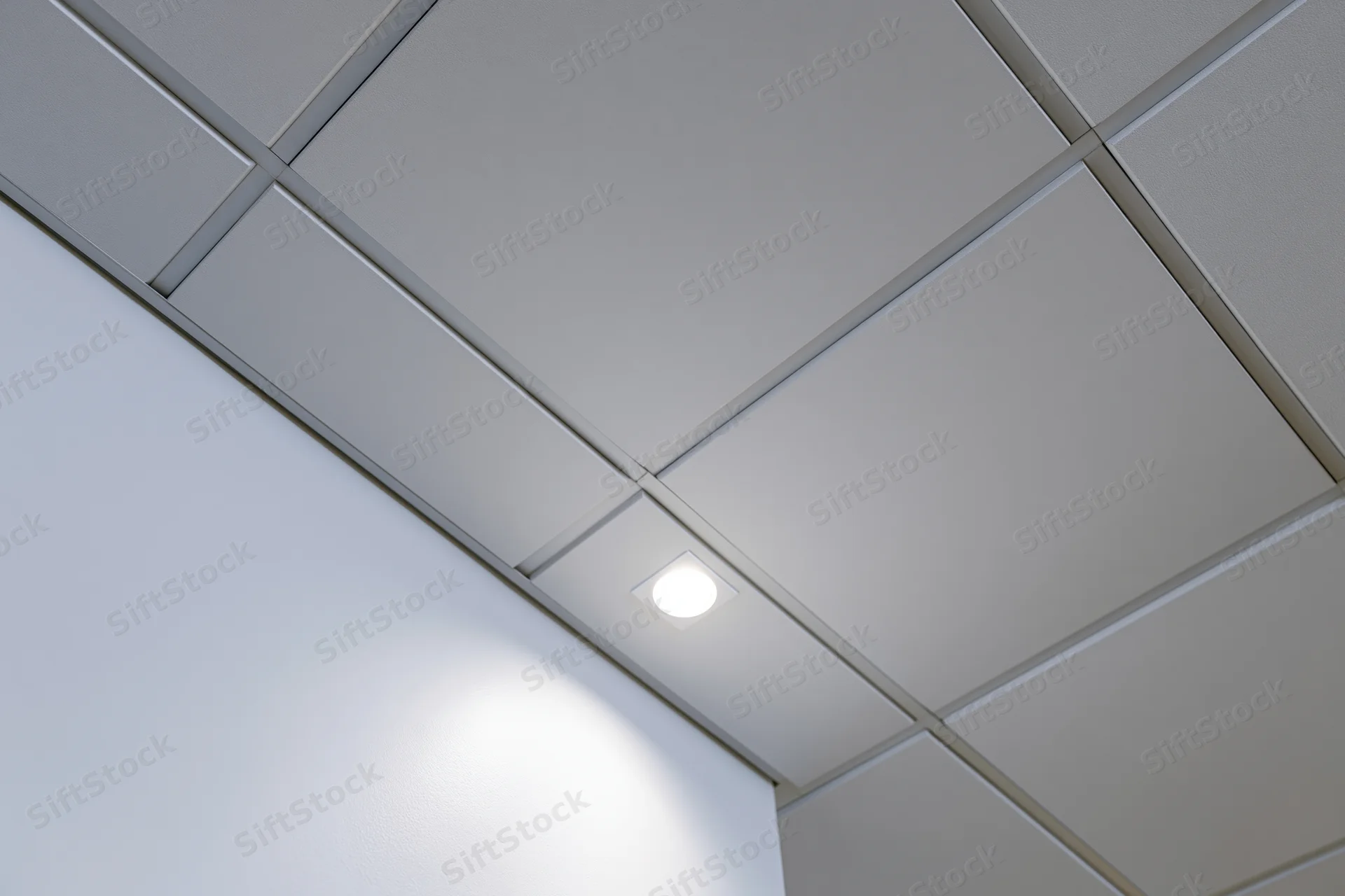 Corner junction of a modern office drop ceiling with recessed lighting and white tiles