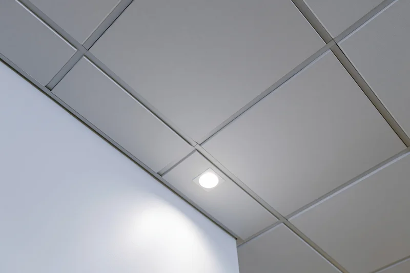 Corner junction of a modern office drop ceiling with recessed lighting and white tiles