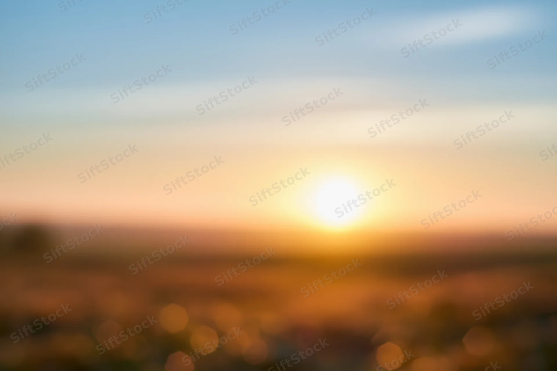 Defocused outdoor scene with bright sun low on the horizon over a blurred landscape at sunset