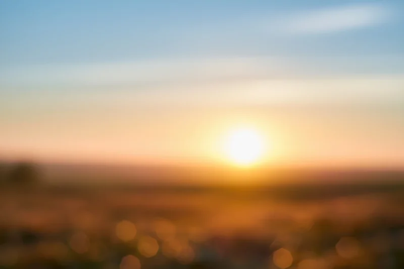 Defocused outdoor scene with bright sun low on the horizon over a blurred landscape at sunset