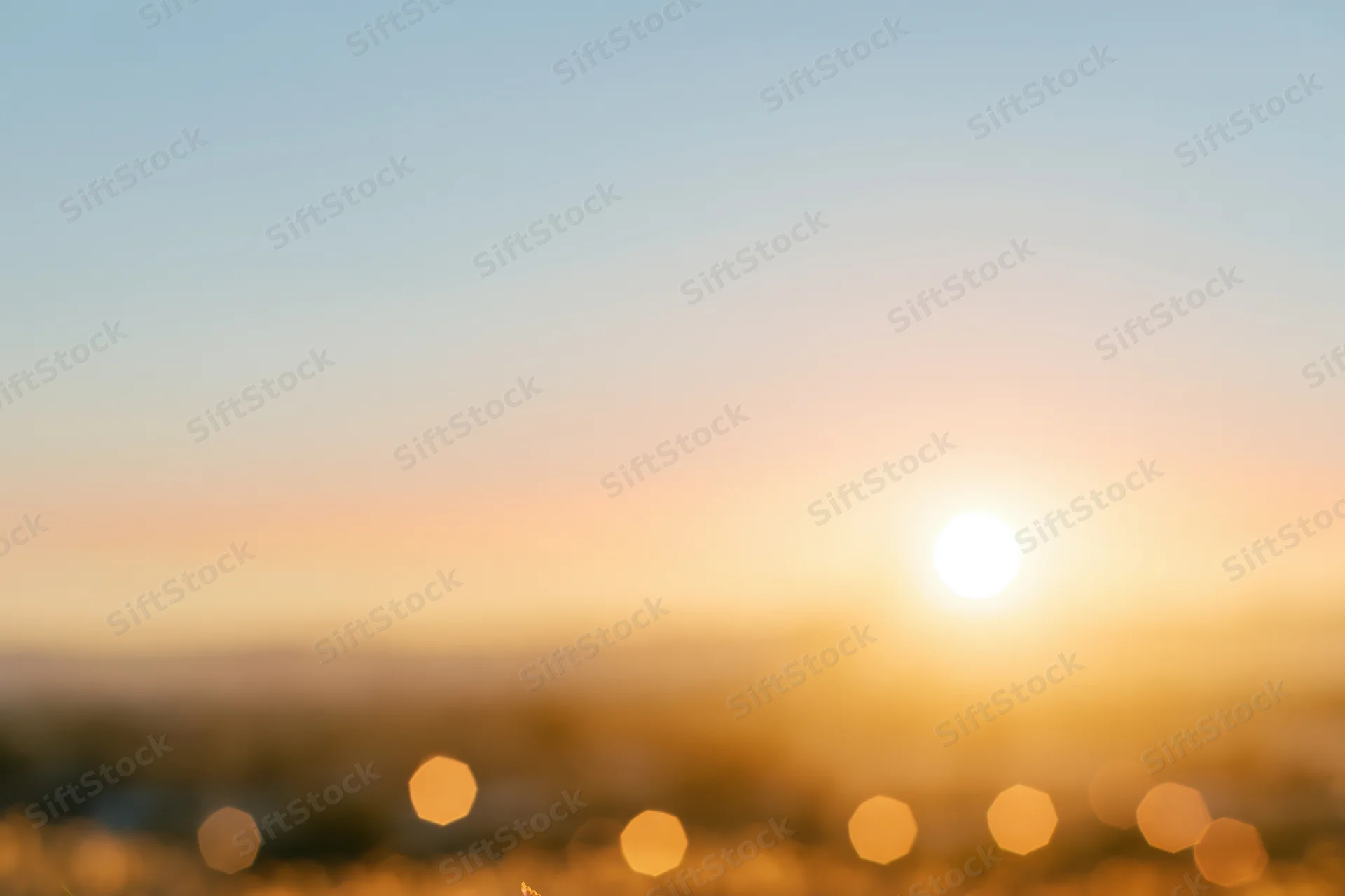 Defocused outdoor scene with bright sun low on the horizon and bokeh lights in foreground