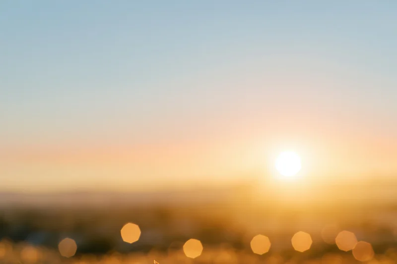 Defocused outdoor scene with bright sun low on the horizon and bokeh lights in foreground