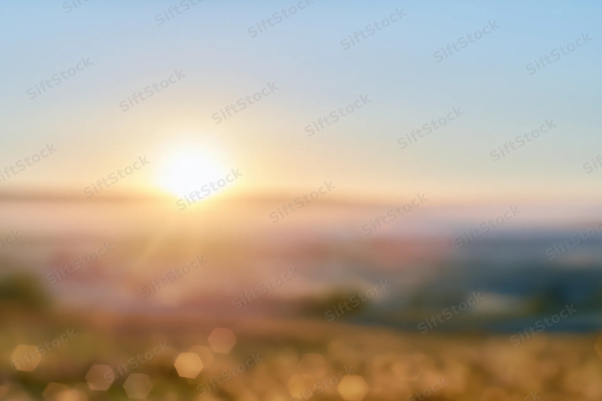 Defocused outdoor scene with bright sun low on the horizon over a blurred landscape at golden hour