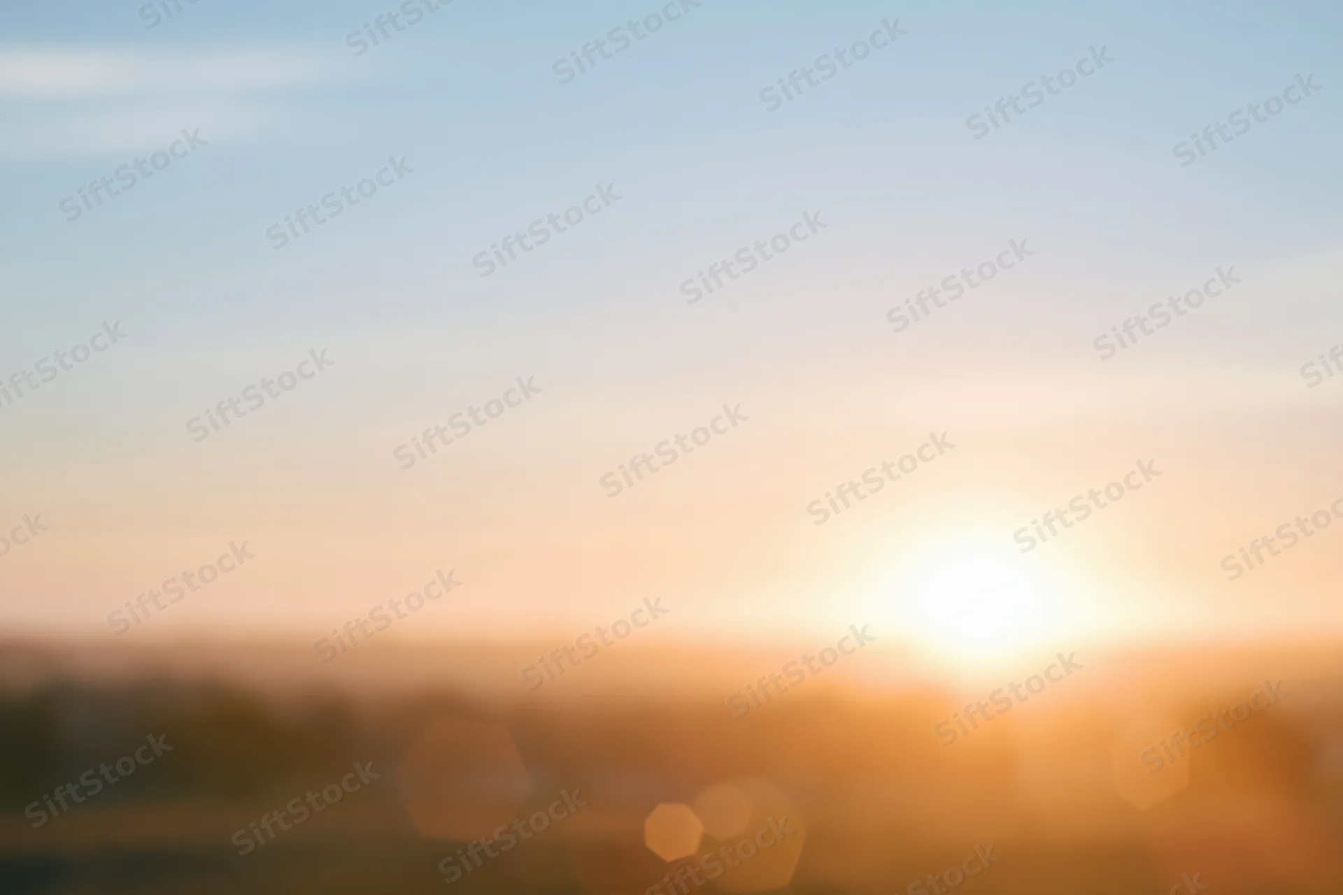 Defocused outdoor scene with bright sun low on the horizon over blurred landscape