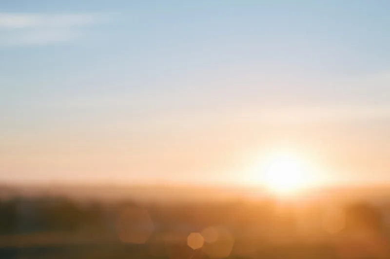Defocused outdoor scene with bright sun low on the horizon over blurred landscape