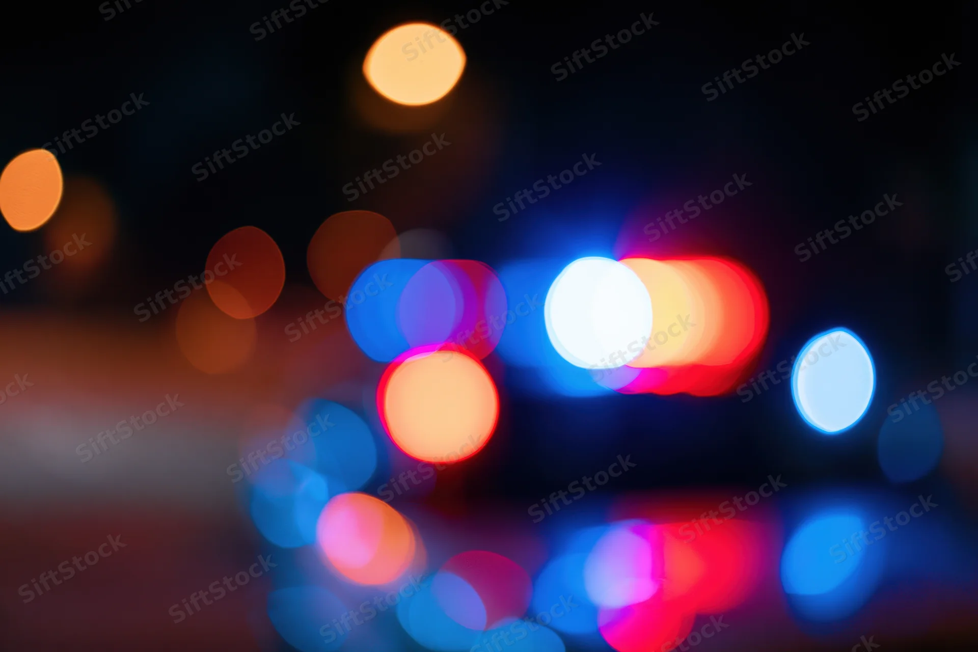 Defocused police emergency lights flashing at night on wet pavement