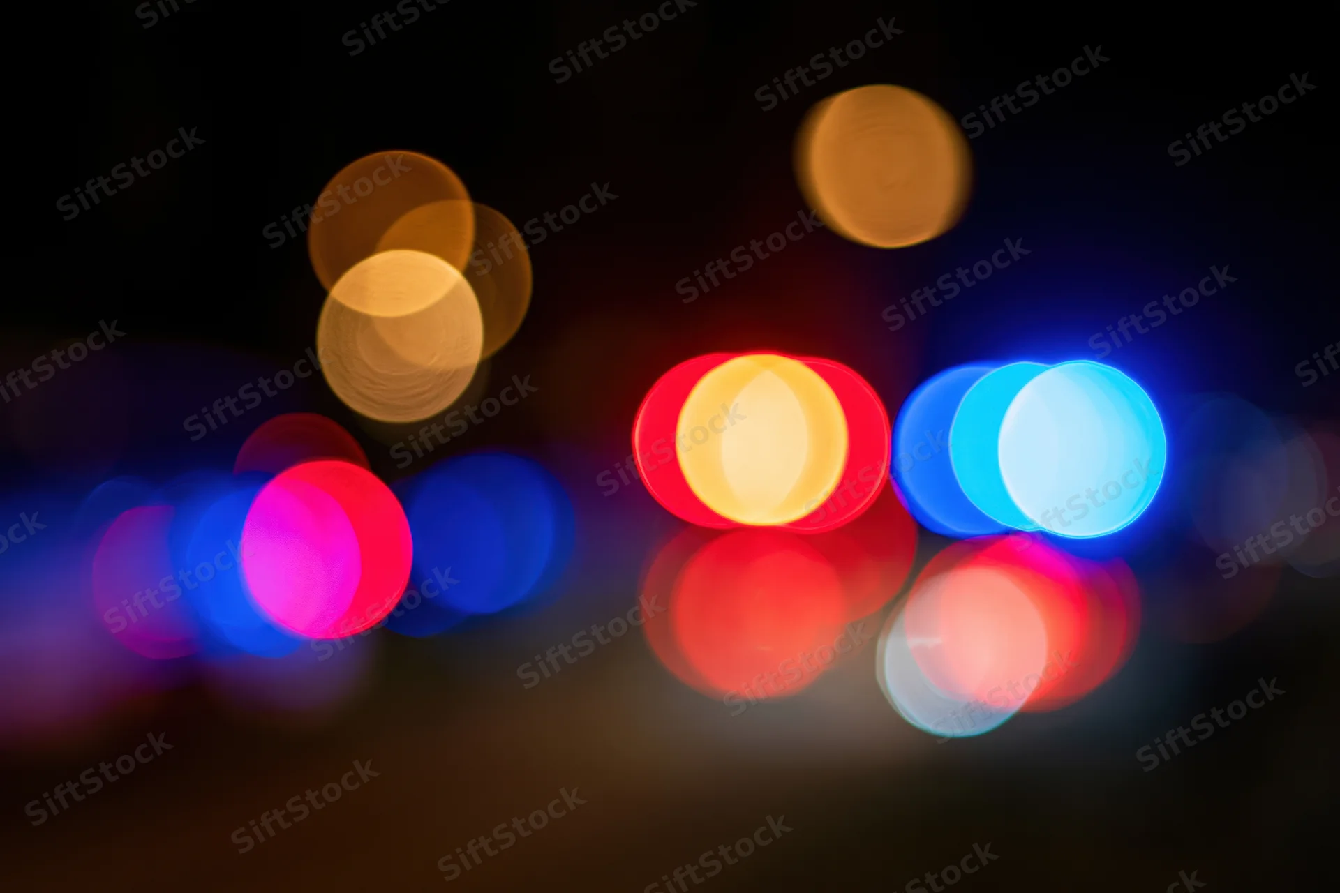 Defocused police car emergency lights flashing at night with bokeh effect and reflections on dark surface