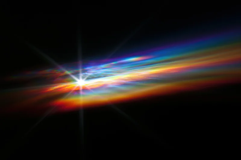 Rainbow light diffraction pattern floating against dark background with starburst glow and color spectrum trails