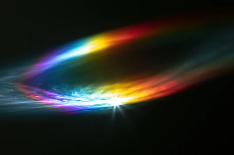 Rainbow light diffraction pattern floating against dark background with bright central glow and colorful arcs