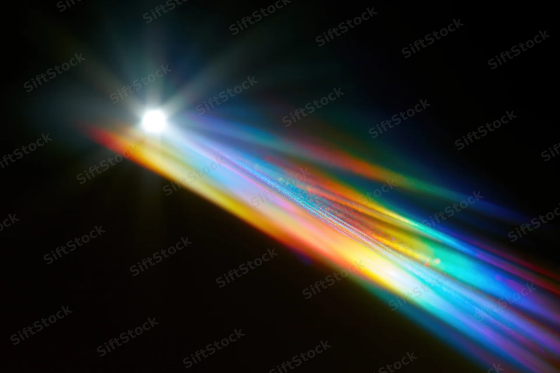Rainbow light diffraction pattern floating against dark background with bright light source and colorful spectrum trails