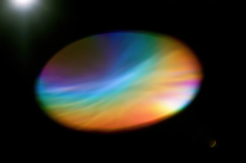 Defocused rainbow light refraction forming an oval bloom against a dark background