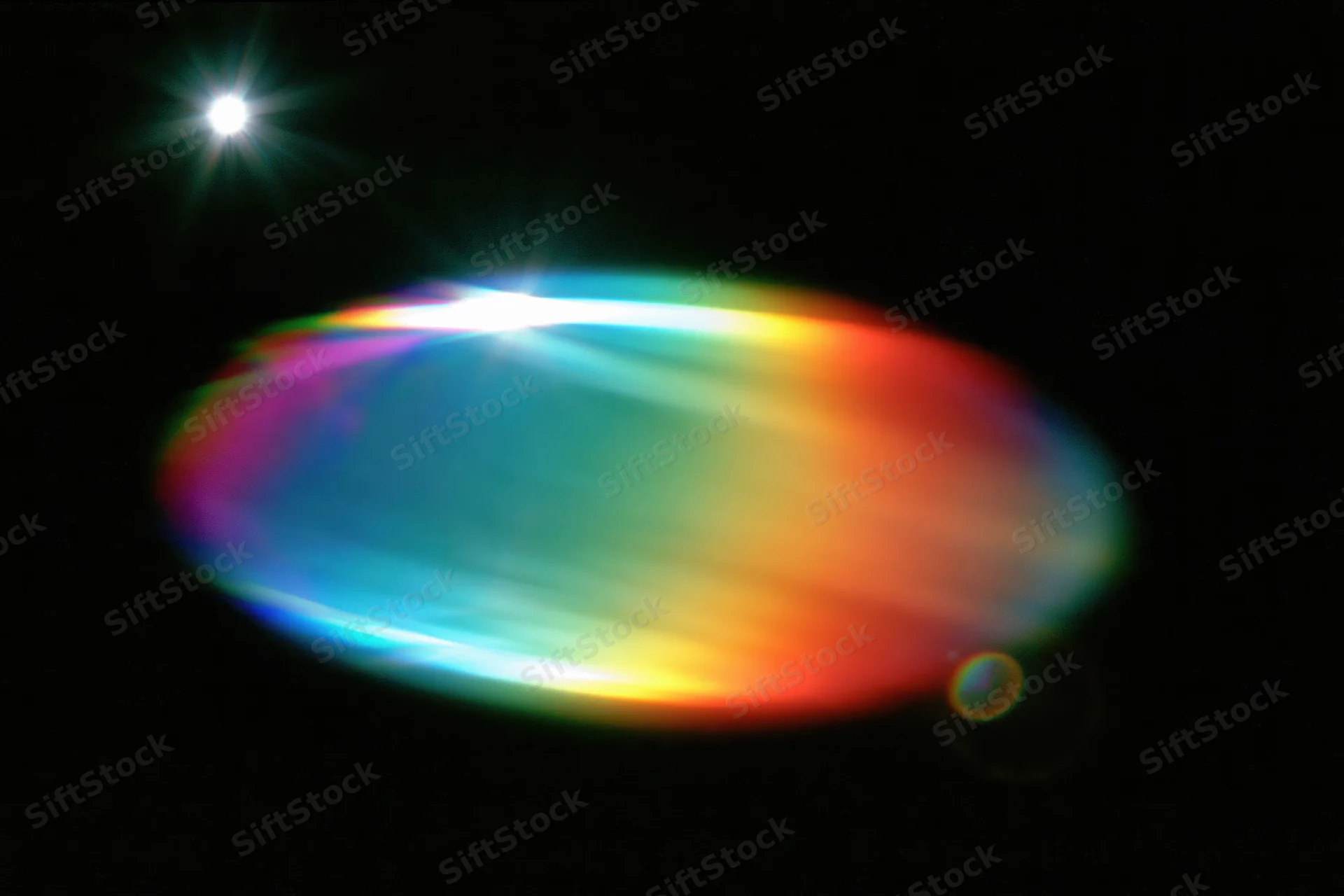 Defocused rainbow light refraction oval bloom floating against dark background with star-like flare