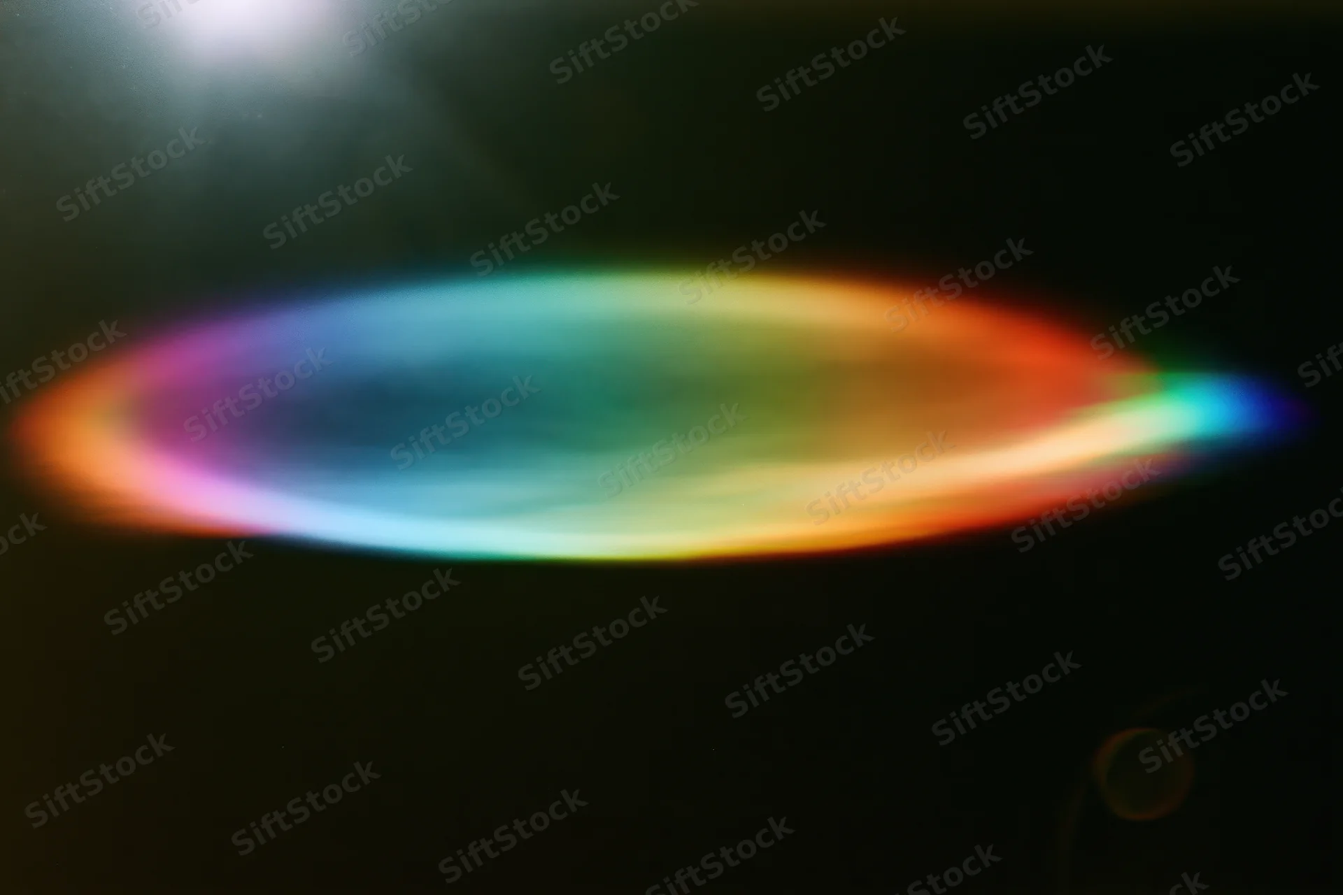 Defocused rainbow light refraction forming an oval bloom against dark background