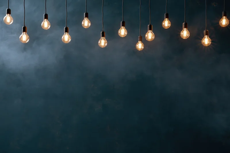Dozen edison bulbs hanging on thin cords across the top of a dark smoky background with copyspace below