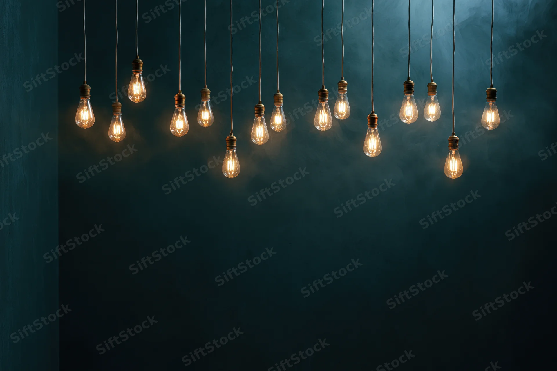 Dozen edison bulbs hanging on thin cords across the upper part of a dark blue wall with copyspace below