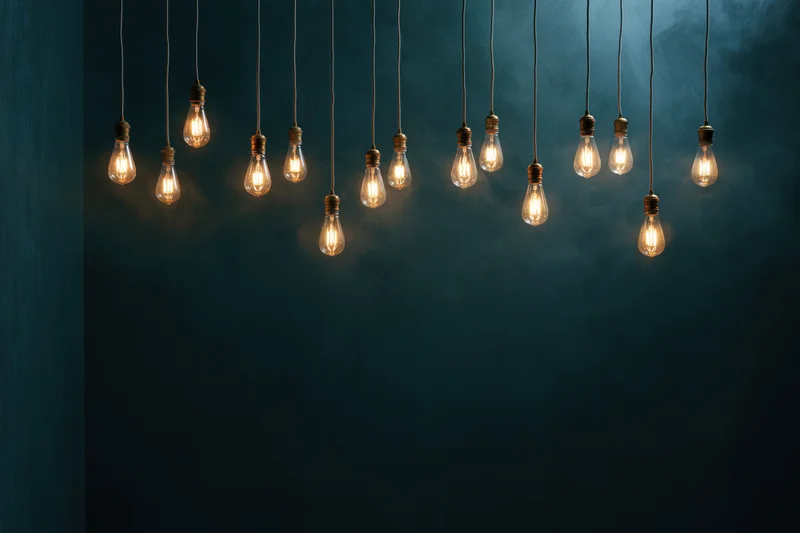 Dozen edison bulbs hanging on thin cords across the upper part of a dark blue wall with copyspace below