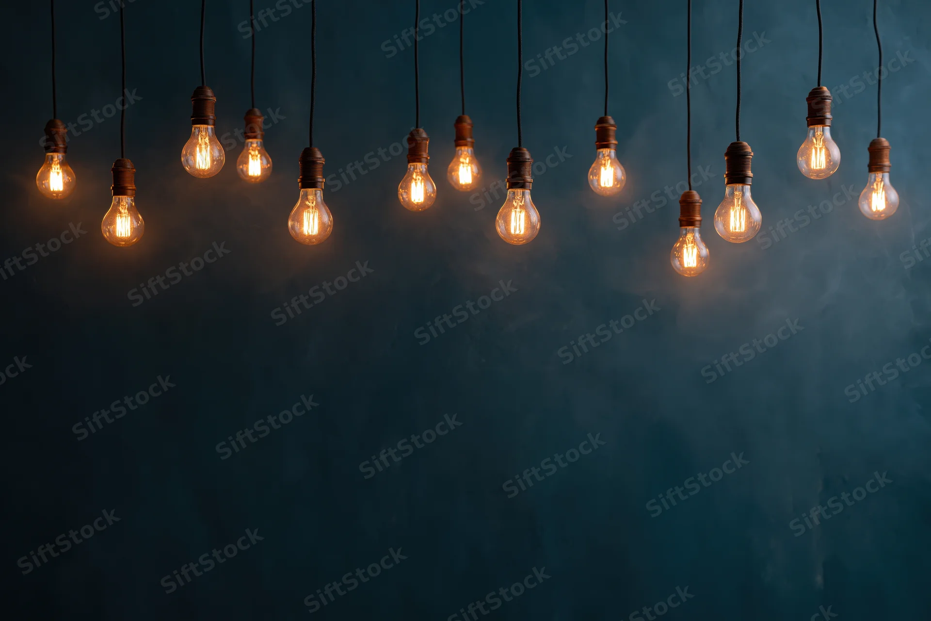 Dozen edison bulbs hanging on thin cords across the upper part of a dark blue textured wall