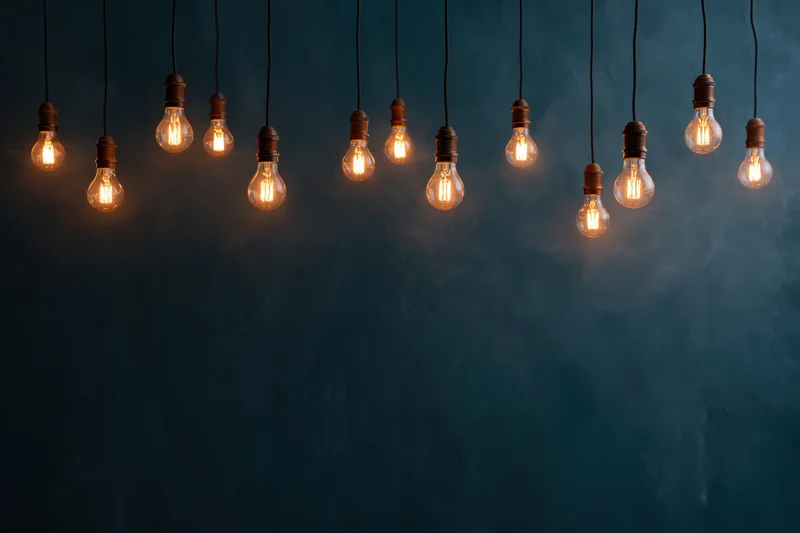 Dozen edison bulbs hanging on thin cords across the upper part of a dark blue textured wall