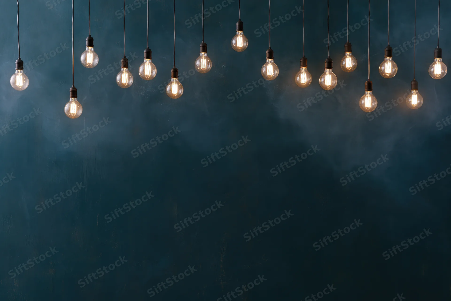 Edison bulbs hanging on thin cords against a dark blue textured wall with copyspace below