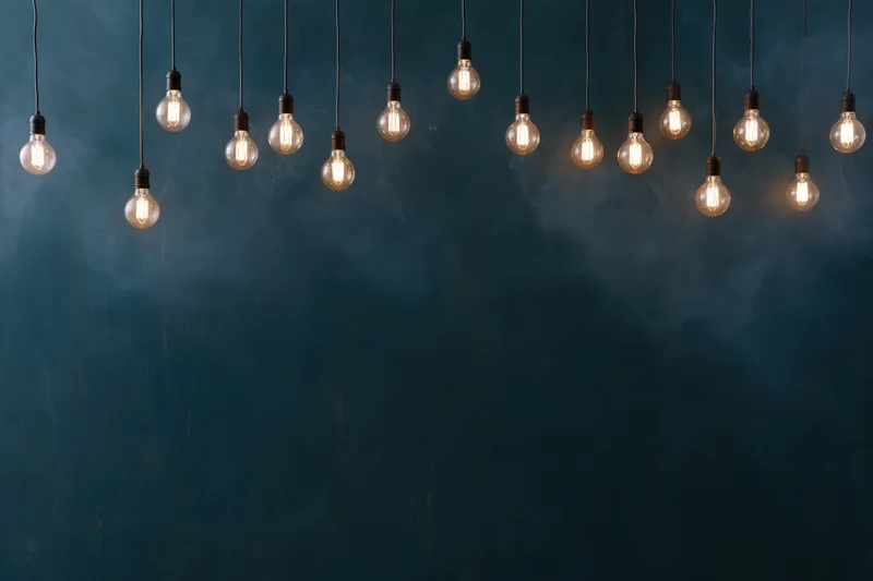 Edison bulbs hanging on thin cords against a dark blue textured wall with copyspace below