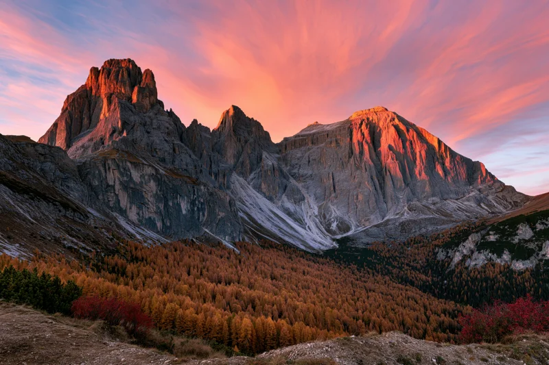 Jagged limestone dolomite peaks at sunset above autumn larch forest in alpine valley
