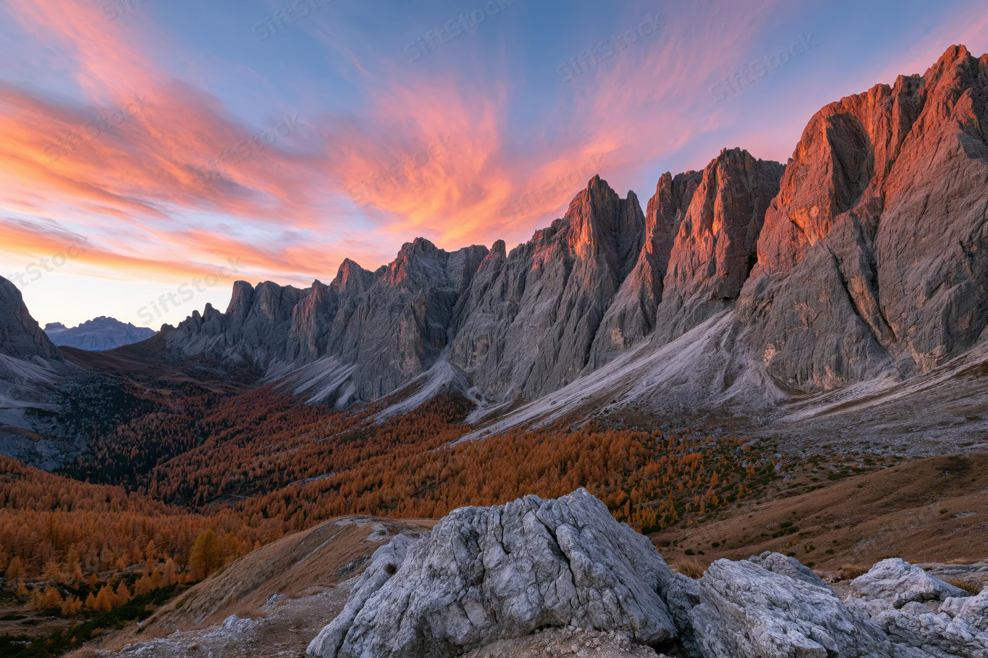 Jagged limestone dolomite peaks at sunset over autumn valley with golden larch forest