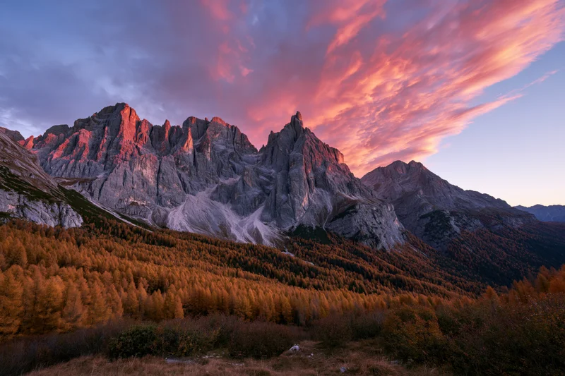 Jagged limestone dolomite peaks at sunset above autumn larch forest in alpine valley