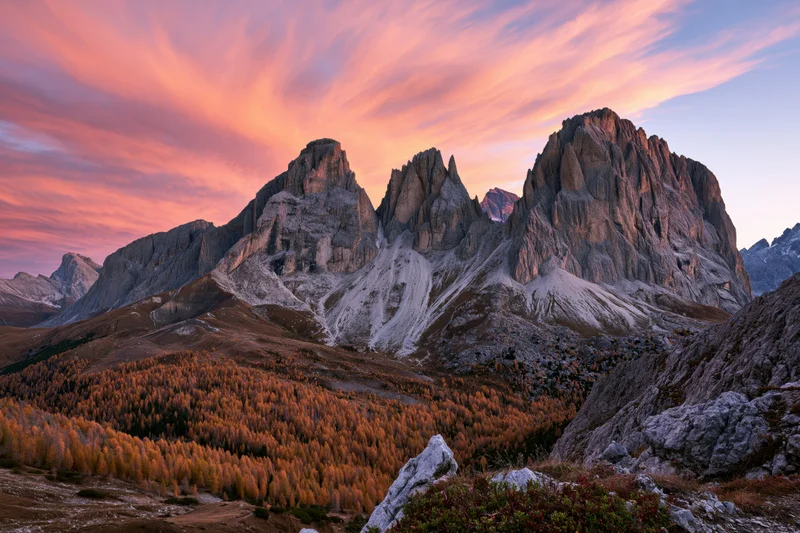 Jagged limestone dolomite peaks at sunset above autumn larch forest in alpine valley