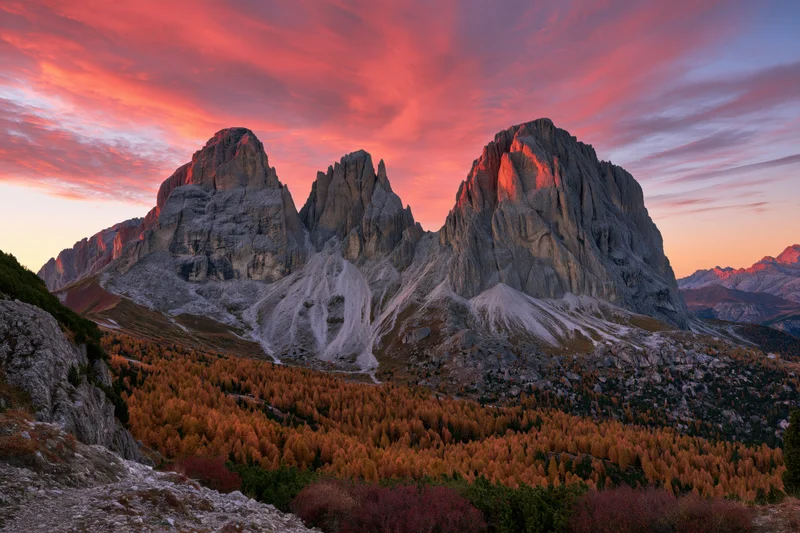 Jagged limestone dolomite peaks at sunset above autumn forest in alpine valley