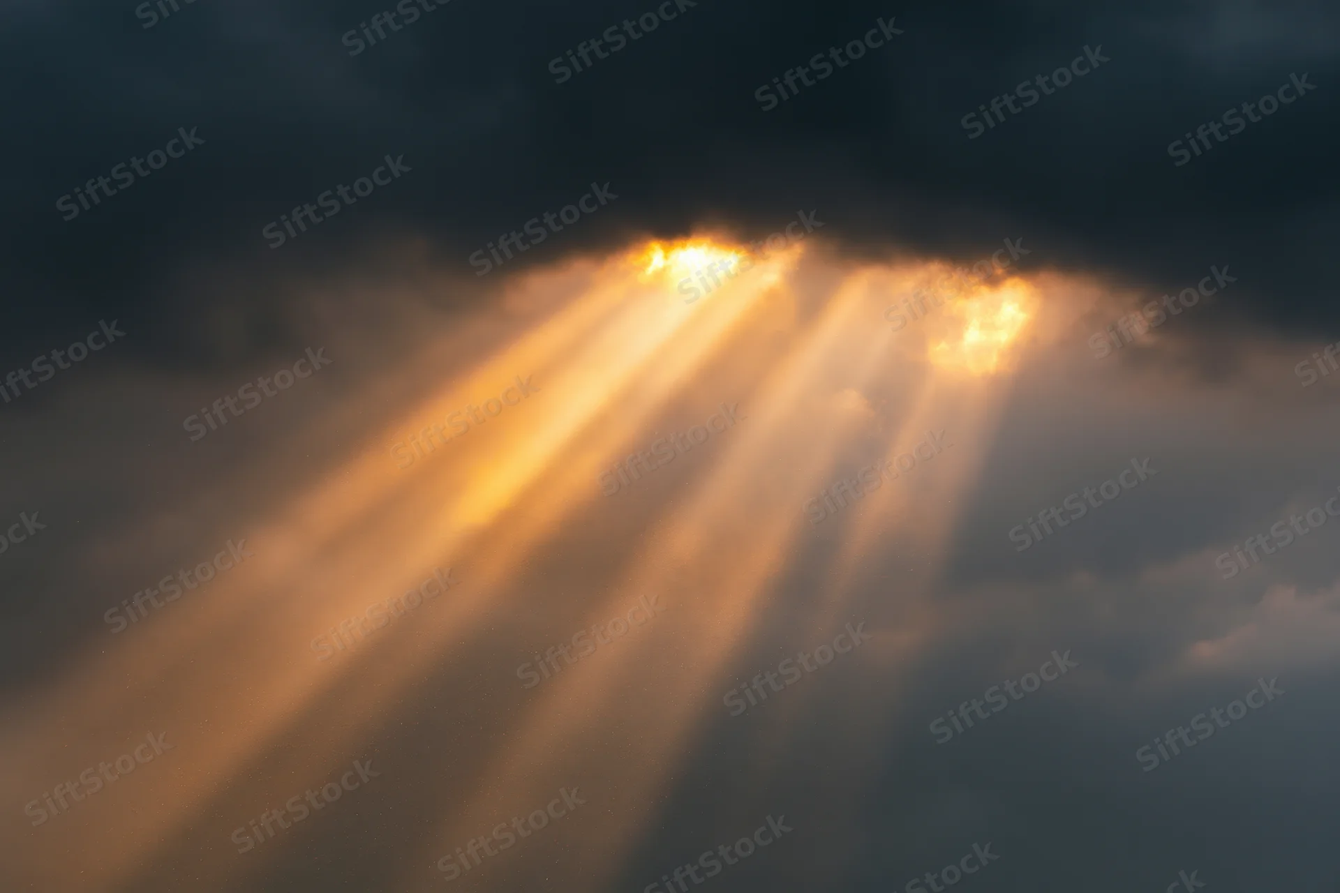 Golden sunbeams breaking through dark storm clouds in the sky