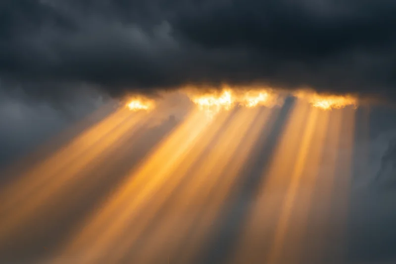 Golden sunbeams breaking through dark storm clouds in the sky