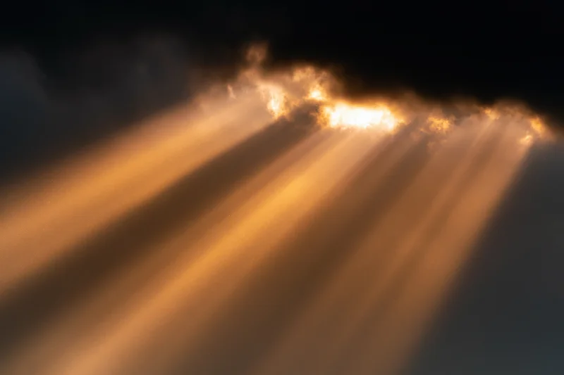 Golden sunbeams breaking through dark storm clouds in the sky