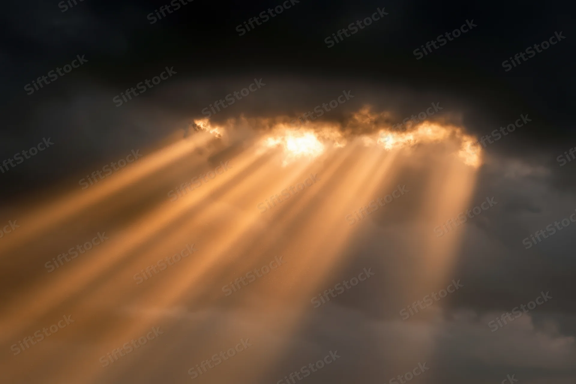 Golden sunbeams breaking through dark storm clouds in the sky