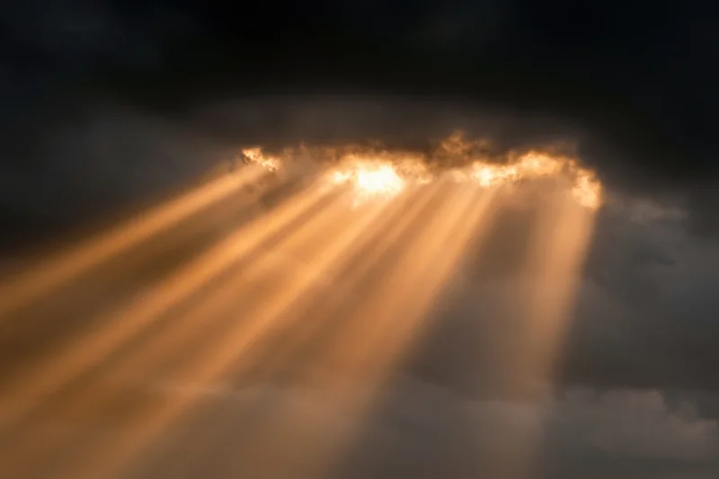 Golden sunbeams breaking through dark storm clouds in the sky
