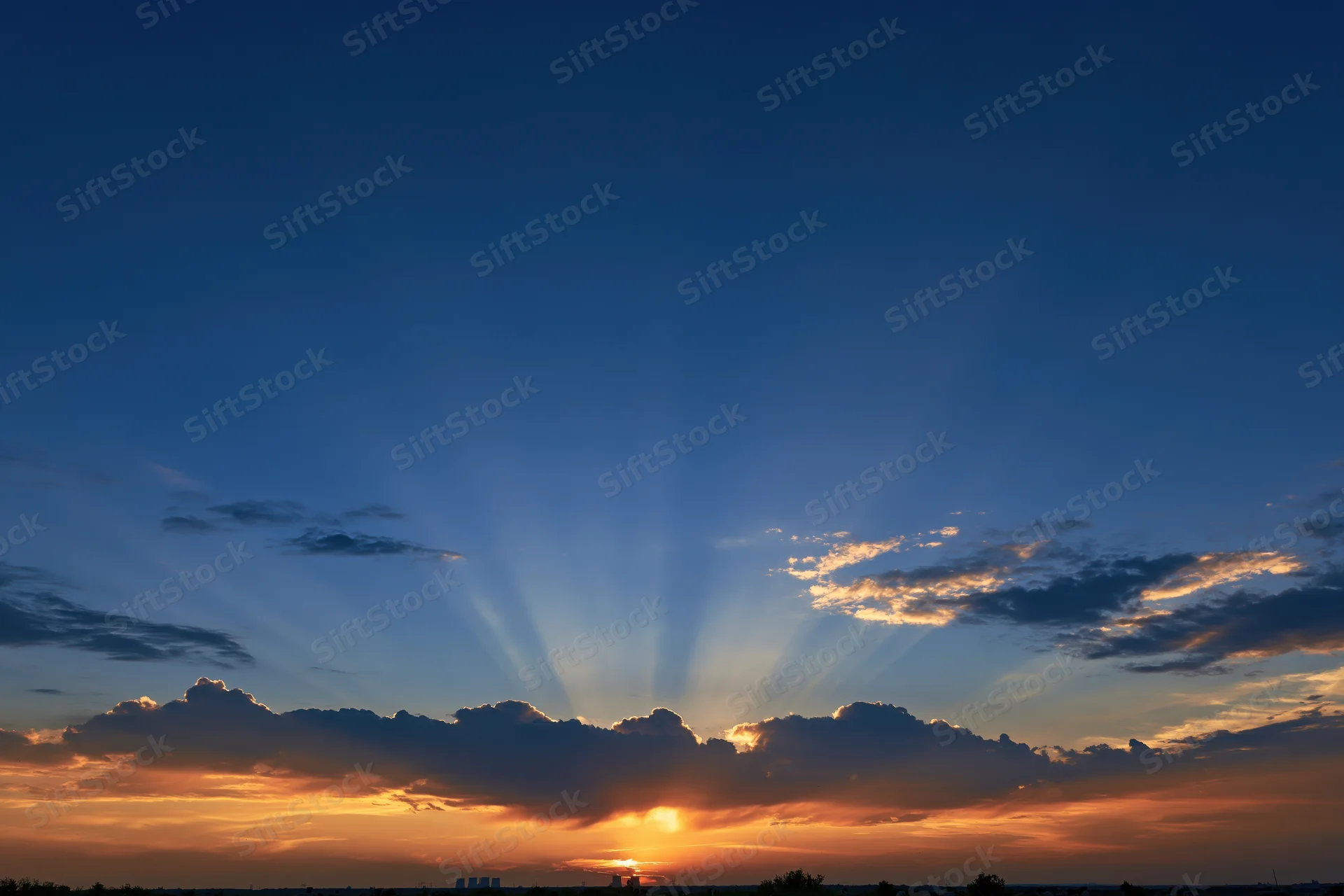 Crepuscular rays bursting upward from sun behind clouds at sunset horizon