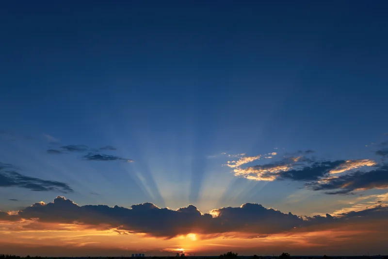 Crepuscular rays bursting upward from sun behind clouds at sunset horizon