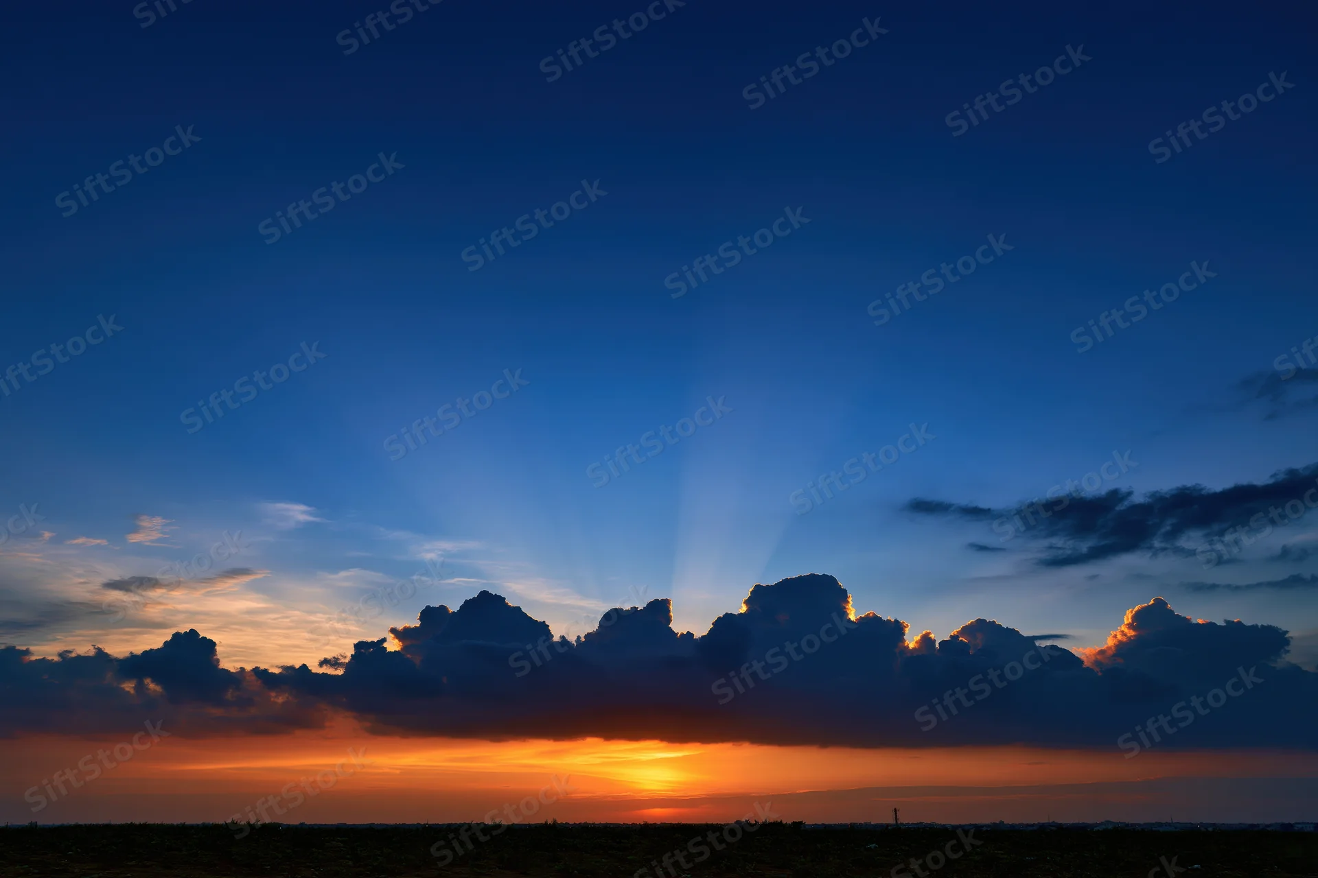 Dramatic sunset sky with crepuscular rays bursting upward from cloud base at horizon