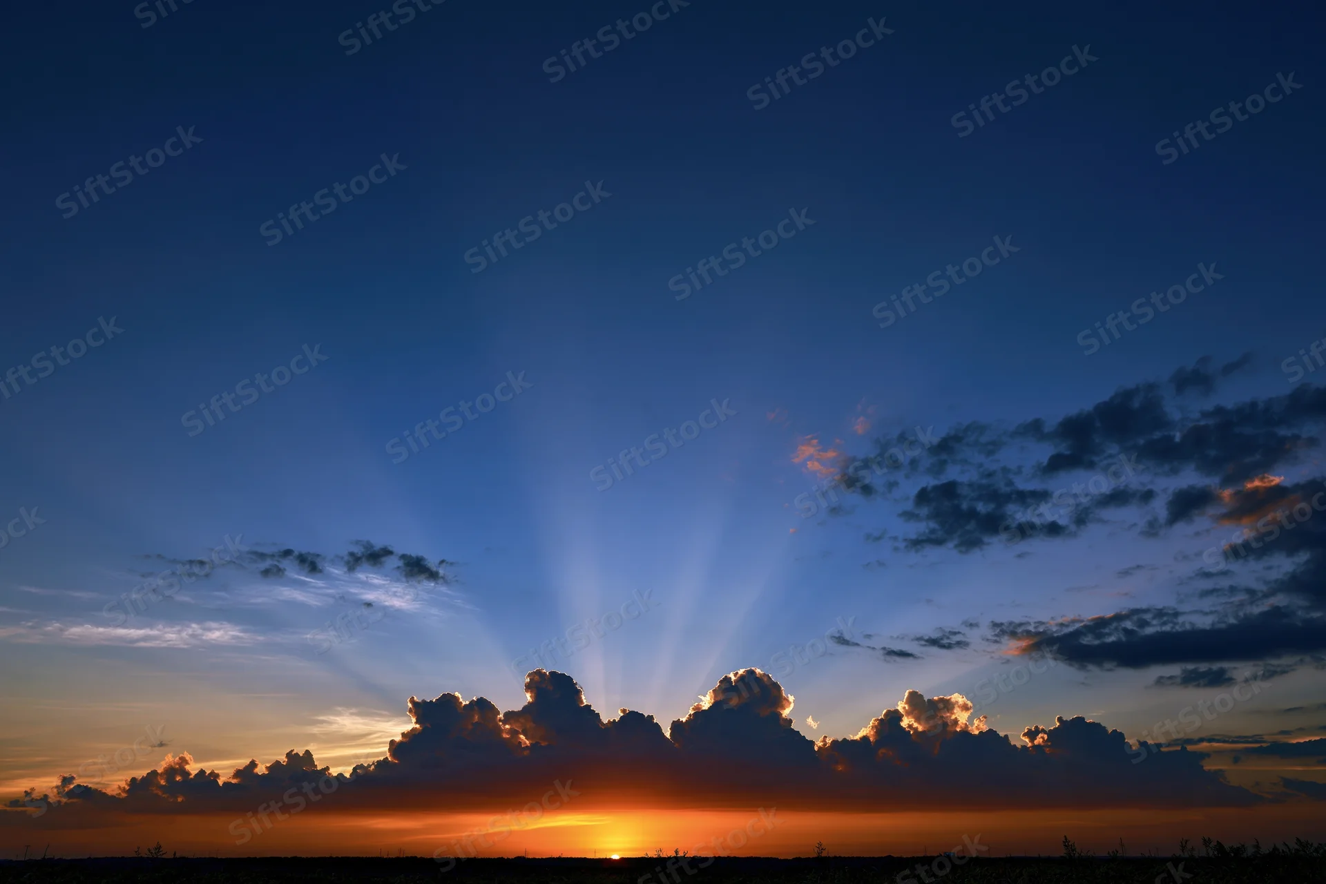 Crepuscular rays bursting upward from clouds at sunset over horizon