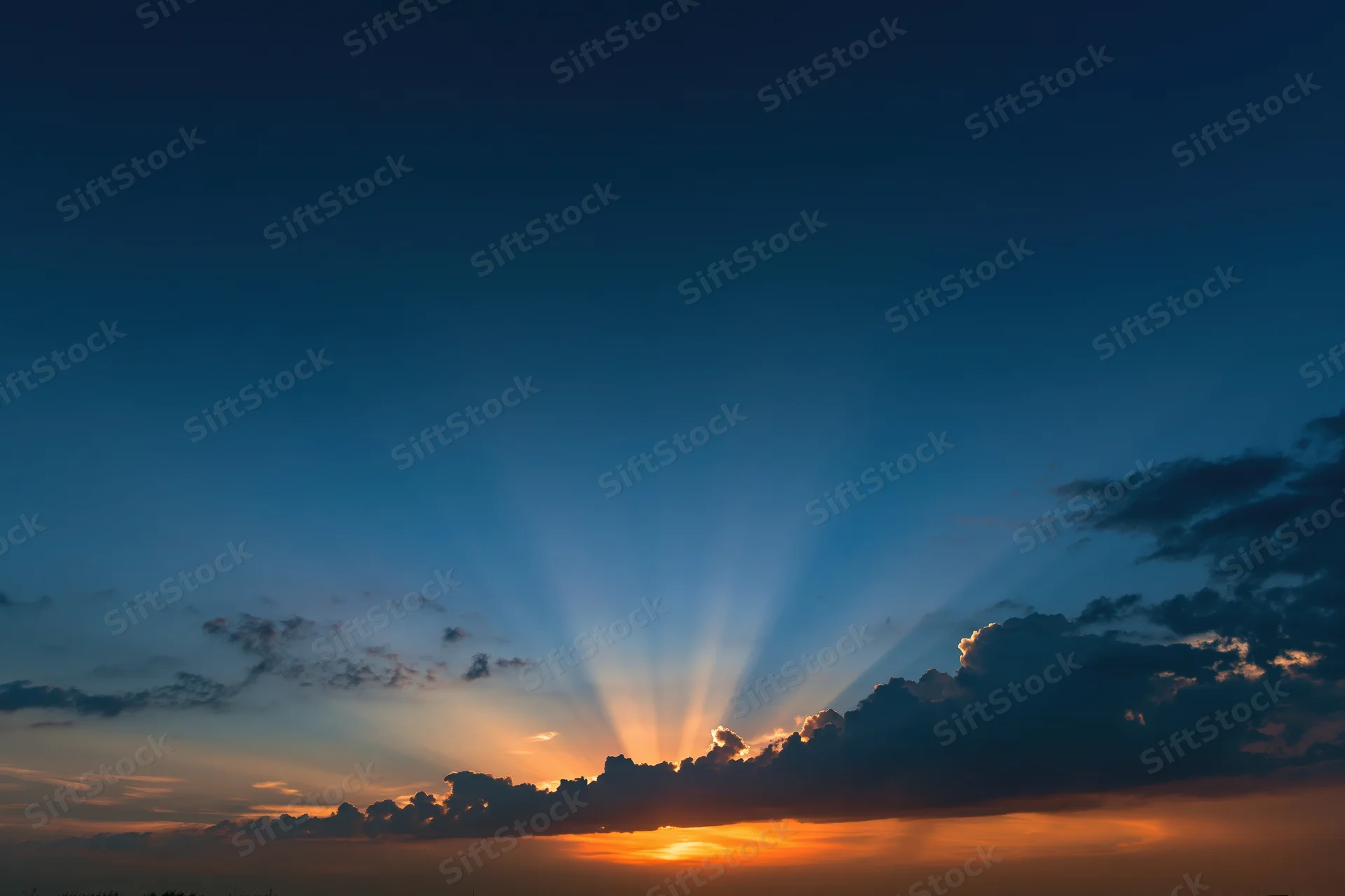 Crepuscular rays bursting upward from clouds at sunset horizon
