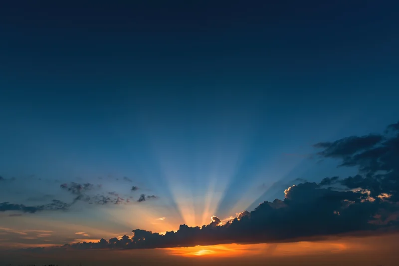 Crepuscular rays bursting upward from clouds at sunset horizon