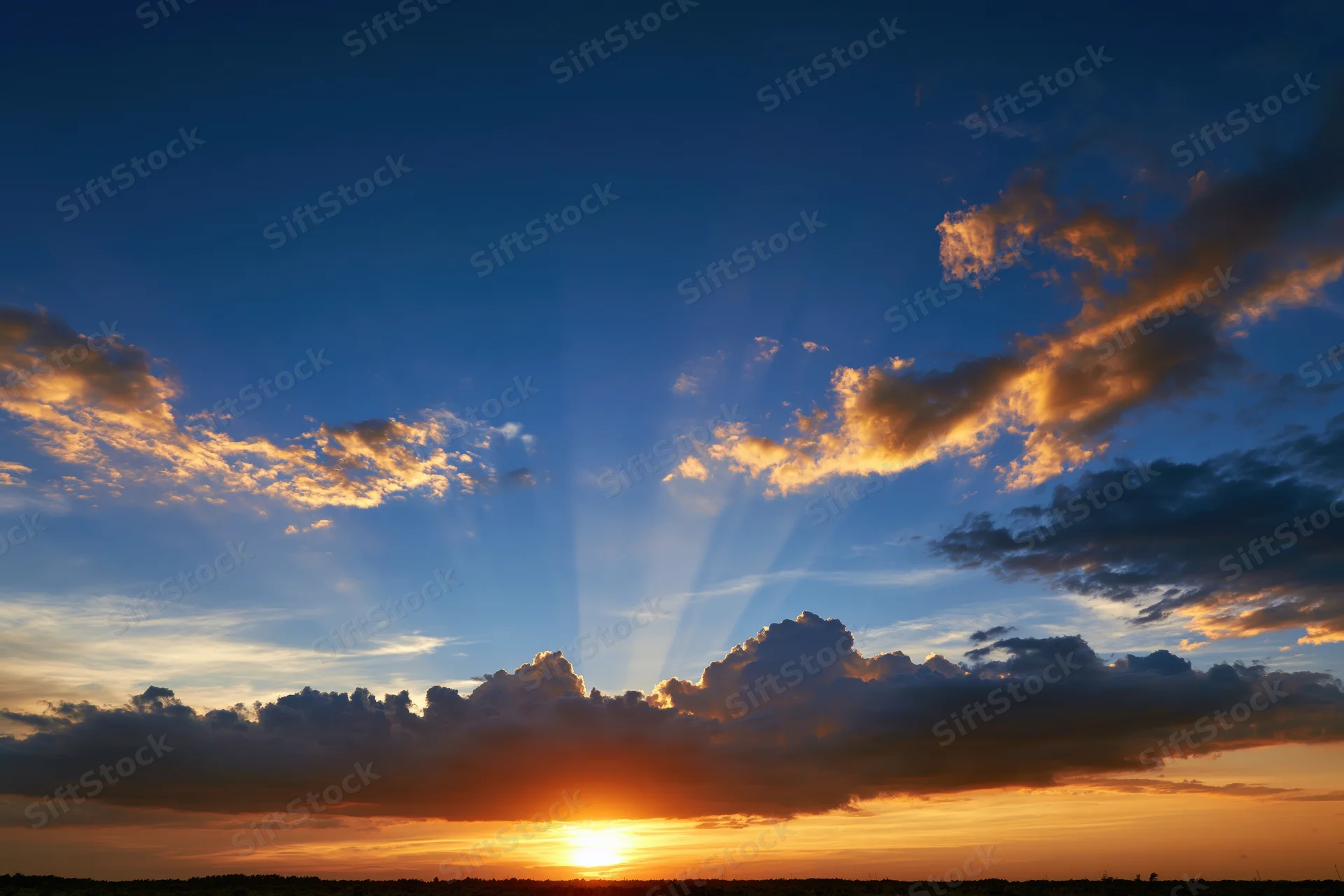 Sunset sky with crepuscular rays bursting upward from behind clouds at horizon