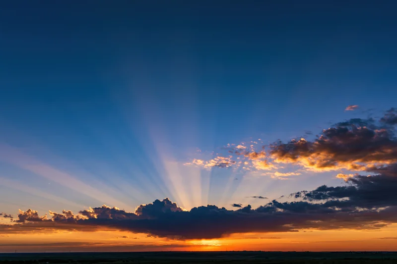 Crepuscular rays bursting upward from clouds at sunset over a flat horizon