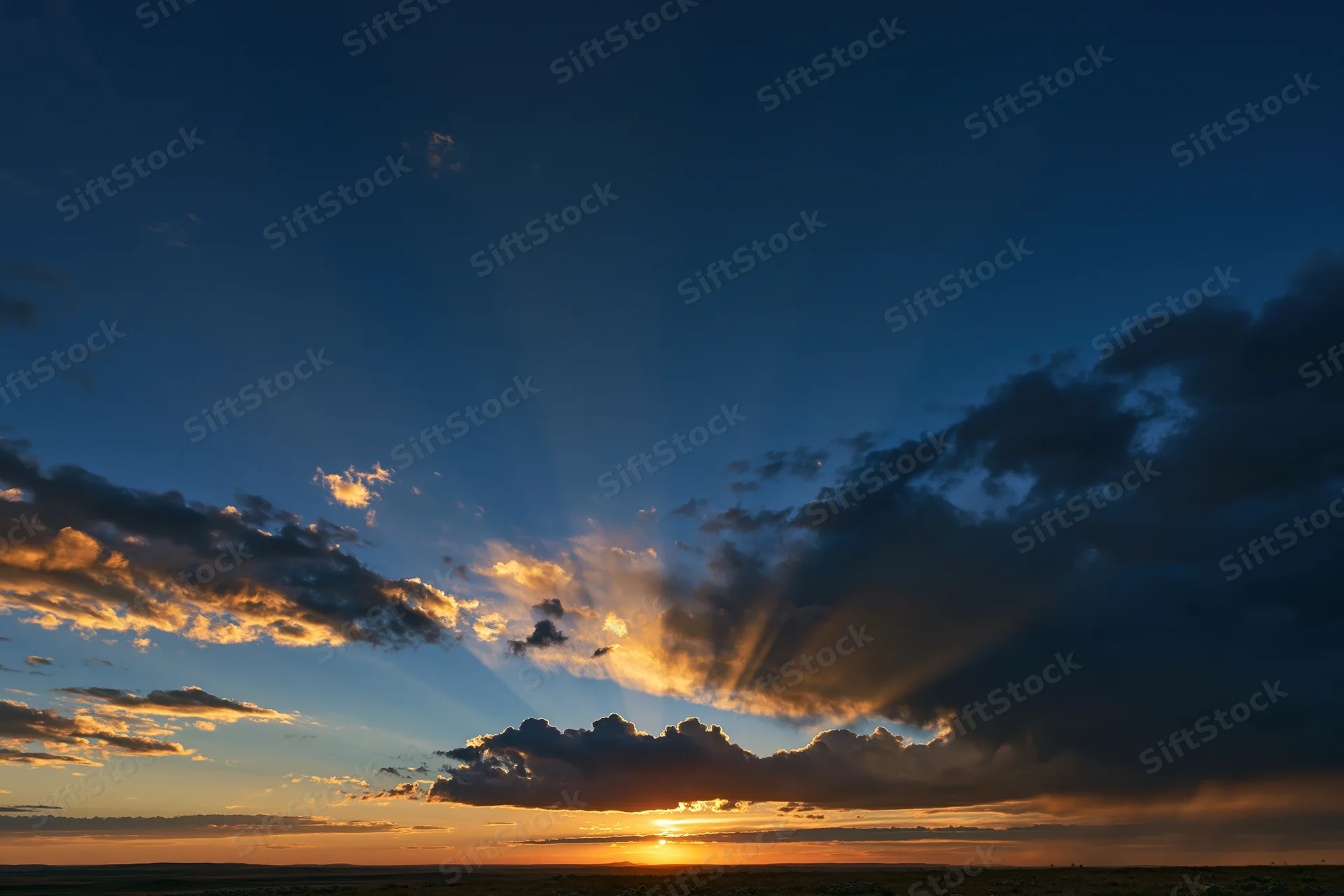Dramatic sunset sky with crepuscular rays bursting upward from horizon over open field