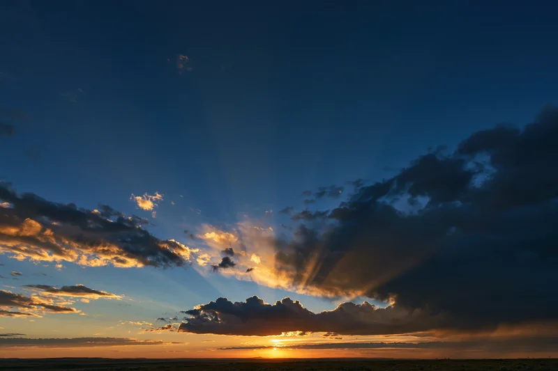 Dramatic sunset sky with crepuscular rays bursting upward from horizon over open field