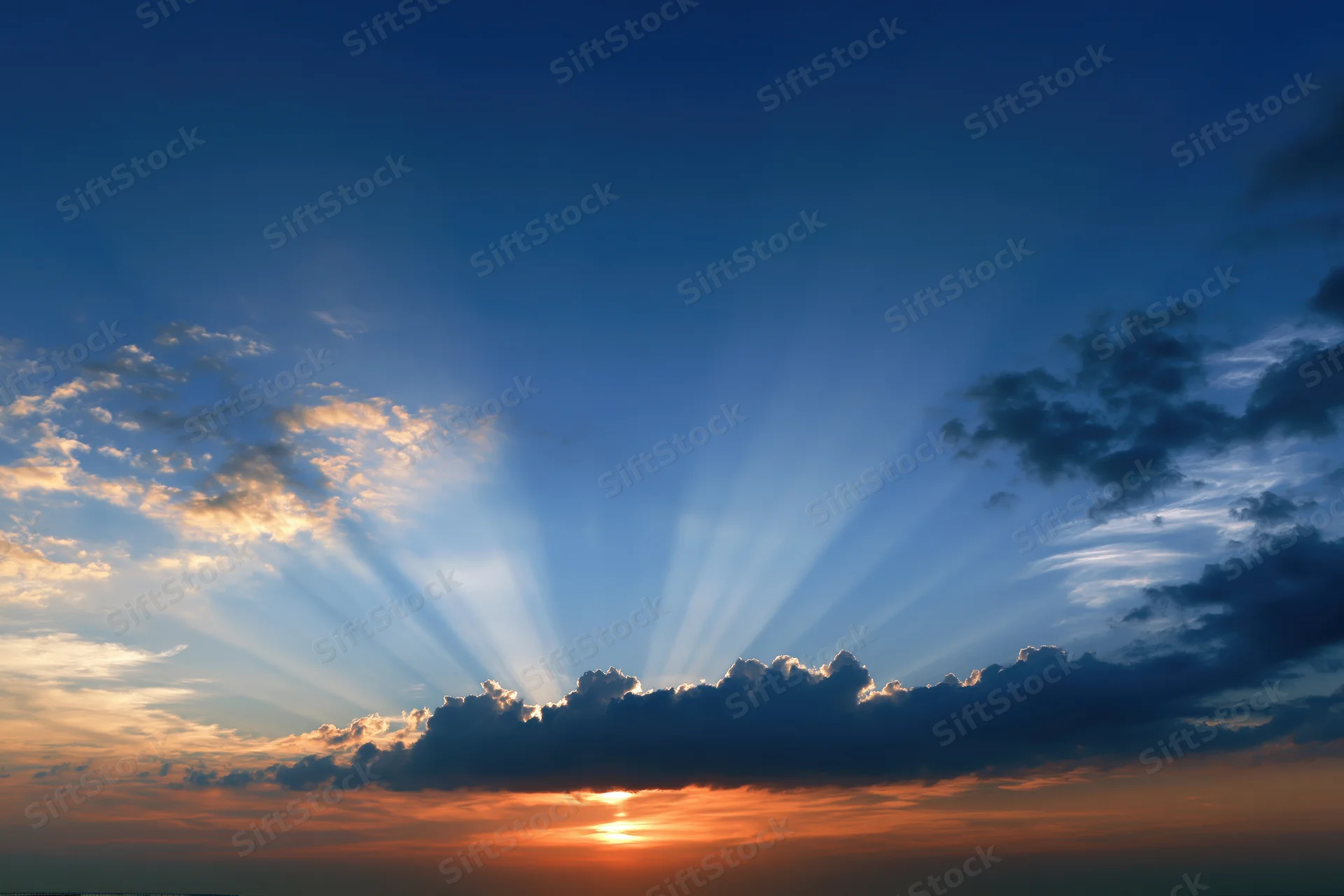 Sunset sky with crepuscular rays bursting upward from clouds at horizon